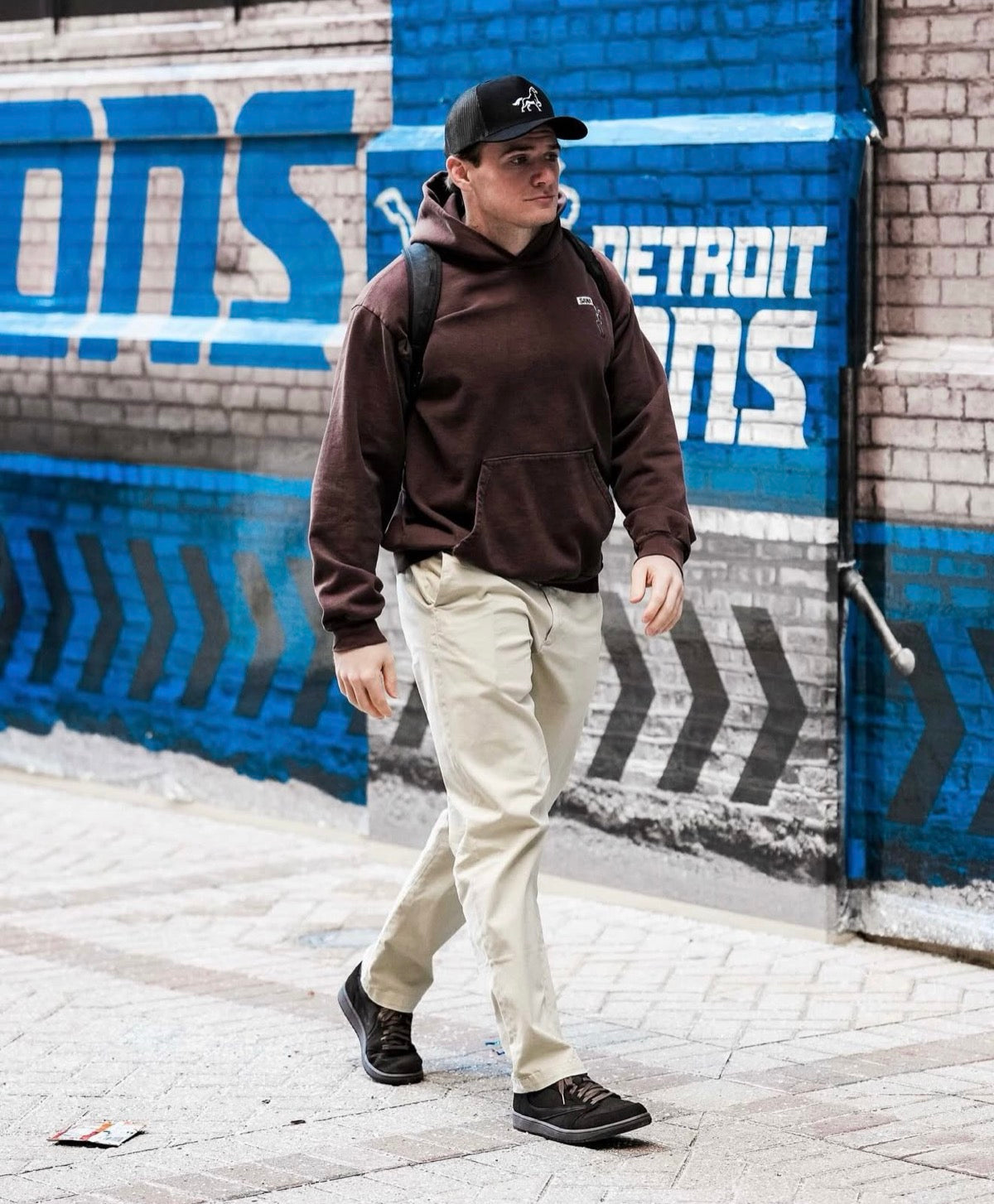 Man wearing an OG STALLY Hat walking with a suitcase and backpack in an urban setting on his way to play for the Detroit Lions