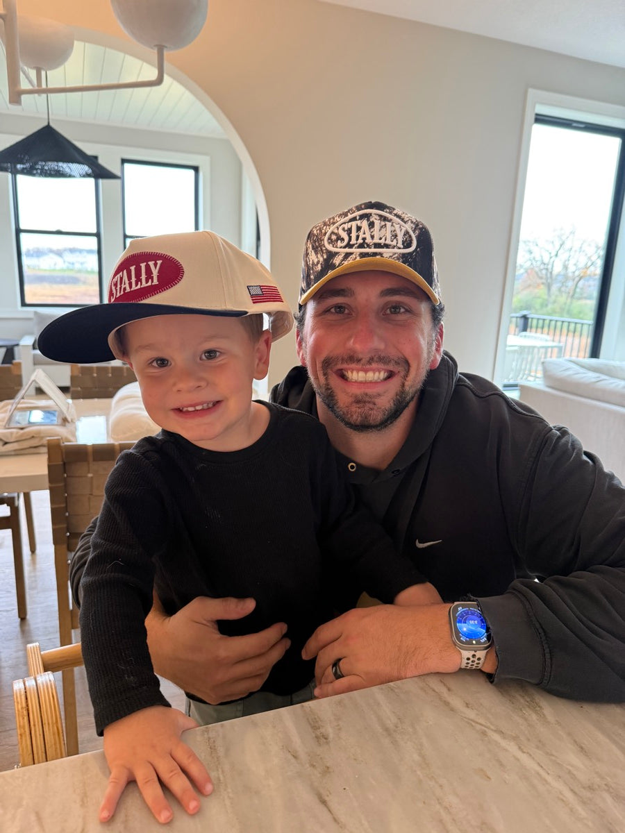 Two people wearing STALLY hats indoors.