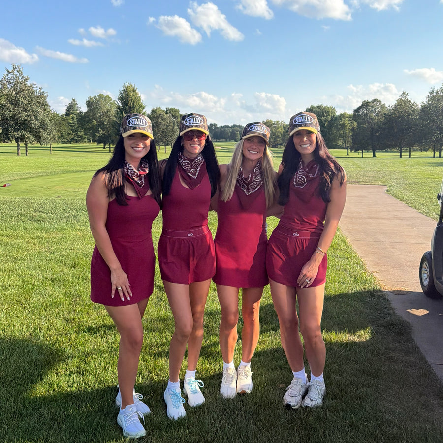 Four friends wearing Stally camo caps on a golf course.