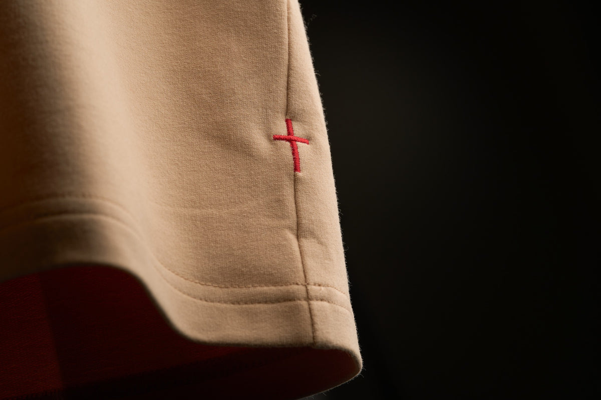 Red embroidered cross on the side seam of a saddlewood Stally tee