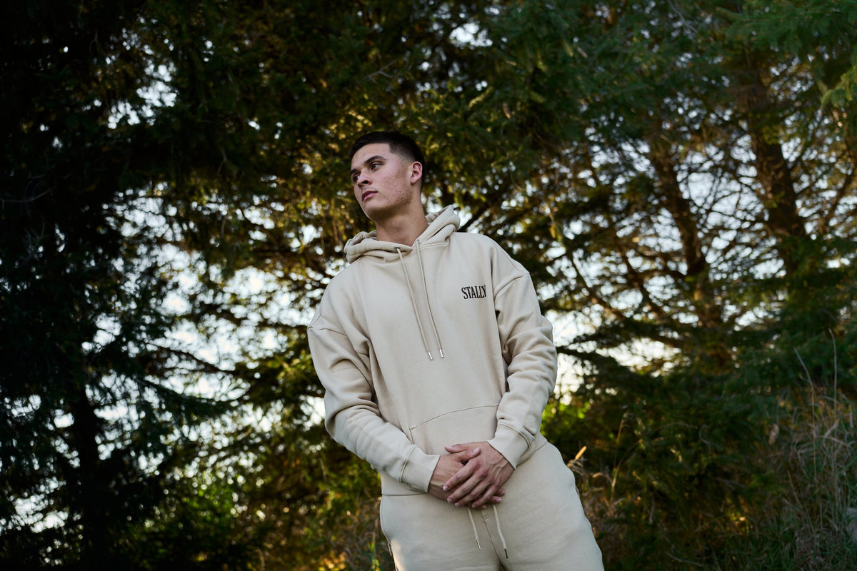 A man in a Saddlewood Stally Draft hoodie and straight leg pants under evergreen trees