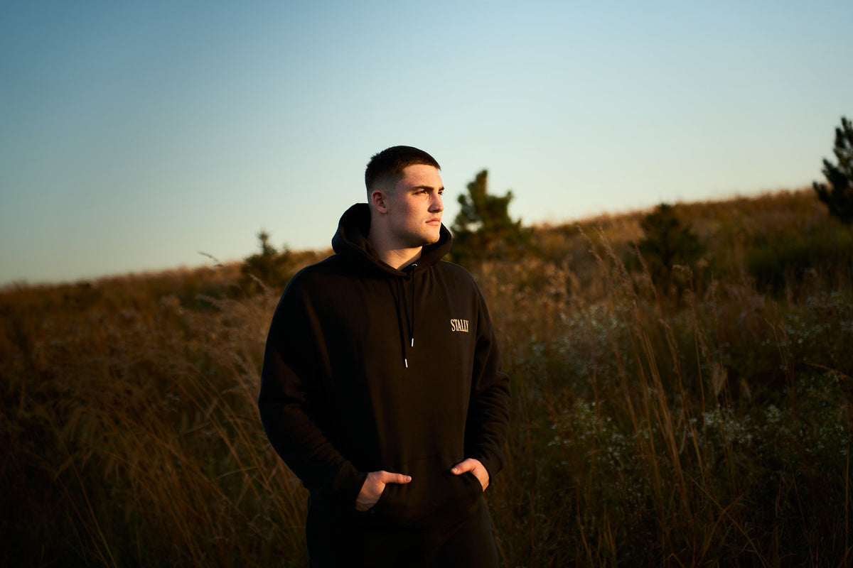 A man in a Coal Black Stally Draft hoodie in a field at dusk