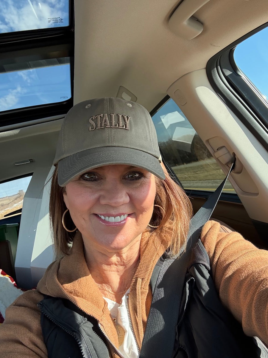 Person wearing a STALLY Heritage Dad Hat and smiling inside a vehicle with a clear sky outside