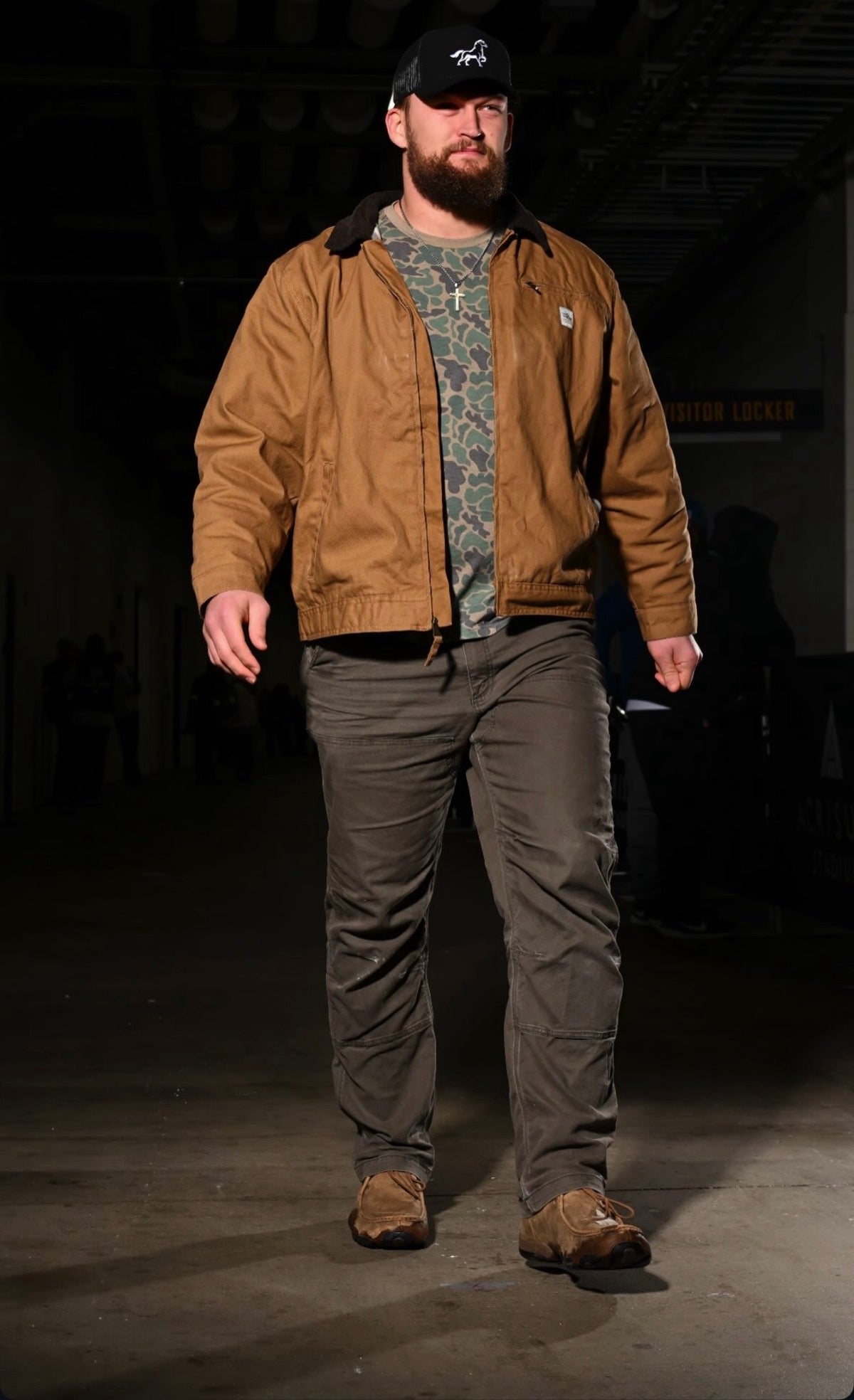 Logan Lee wearing a brown jacket and OG STALLY hat in a dark setting on his way to an NFL game for the Steelers