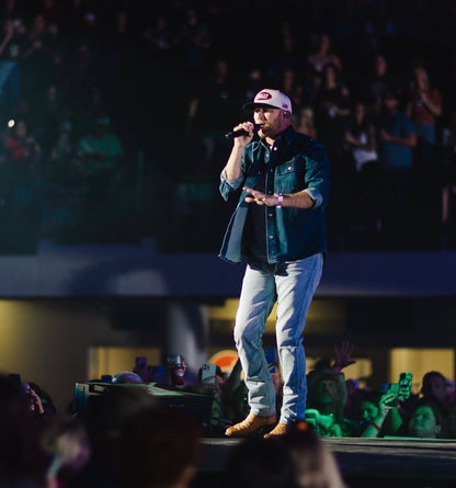 Cole Swindell on stage wearing an All American STALLY hat with microphone in front of an audience