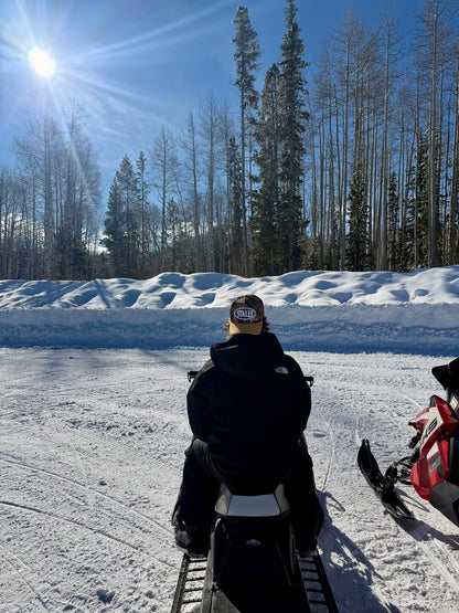 Man sitting on a snowmobile wearing Camo STALLY Hat backwards.