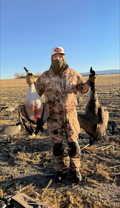 Hunter holding 2 geese wearing an All American STALLY hat.