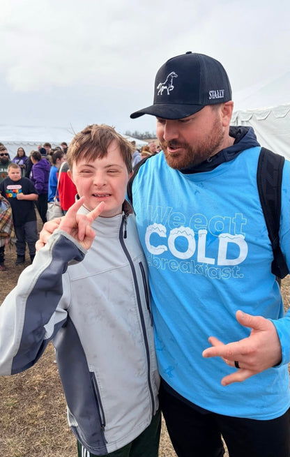 Two people standing together outdoors. One is the NFL player Harrson Philips with a crowd in the background, one wearing an OG STALLY hat