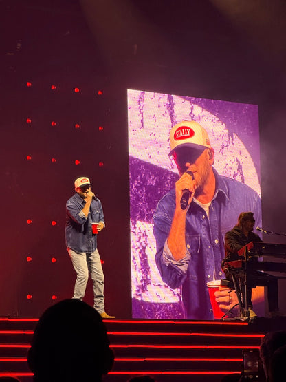 Two musicians on stage. Cole Swindell wearing an All American STALLY hat