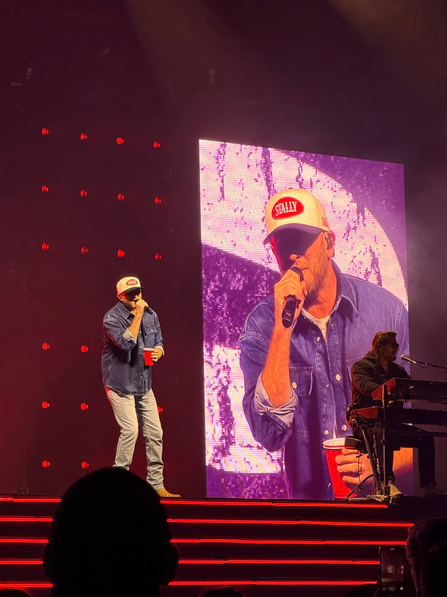 Two musicians on stage. Cole Swindell wearing an All American STALLY hat