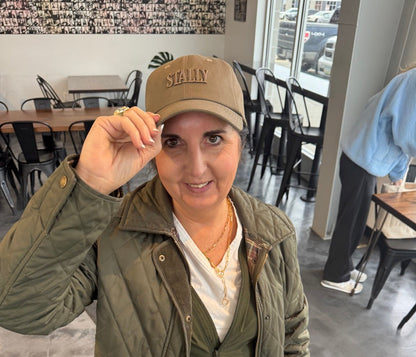 Person wearing a green jacket and STALLY Heritage Dad Hat sitting on a chair indoors.