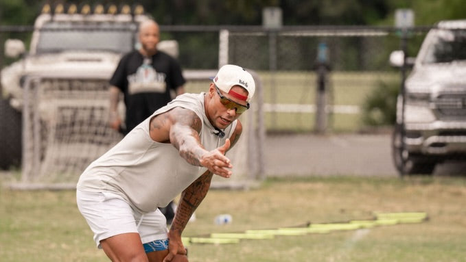 A man in a backward white cap reaching forward during an outdoor field activity.