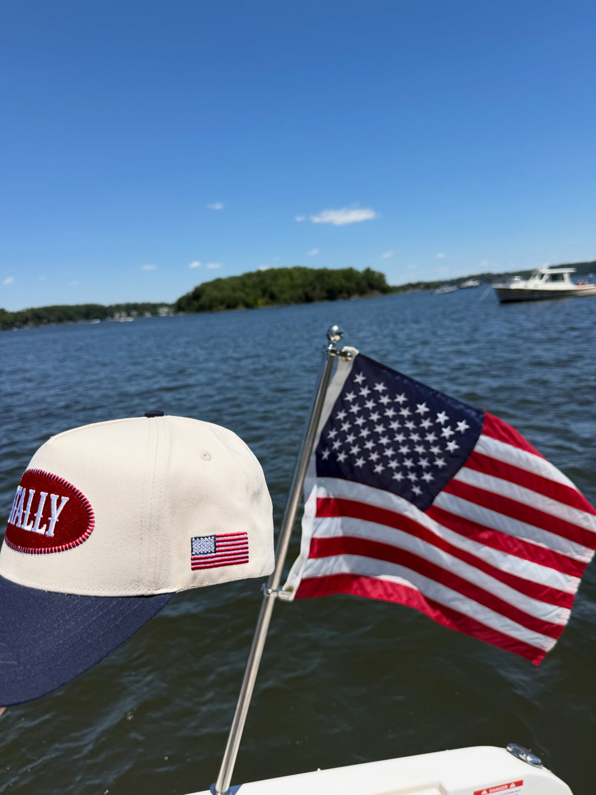 A Stally cap beside an American flag on a boat, open water and an island behind