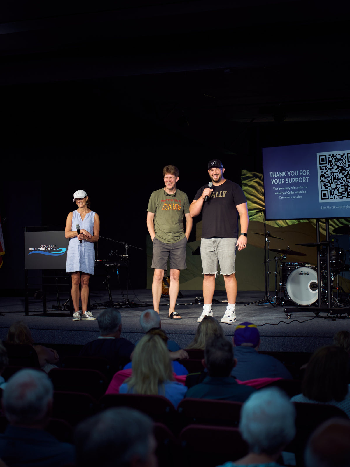 Ike and two others on the stage at Cedar Falls Bible Conference, facing the congregation, beside a screen that reads Thank you for your support