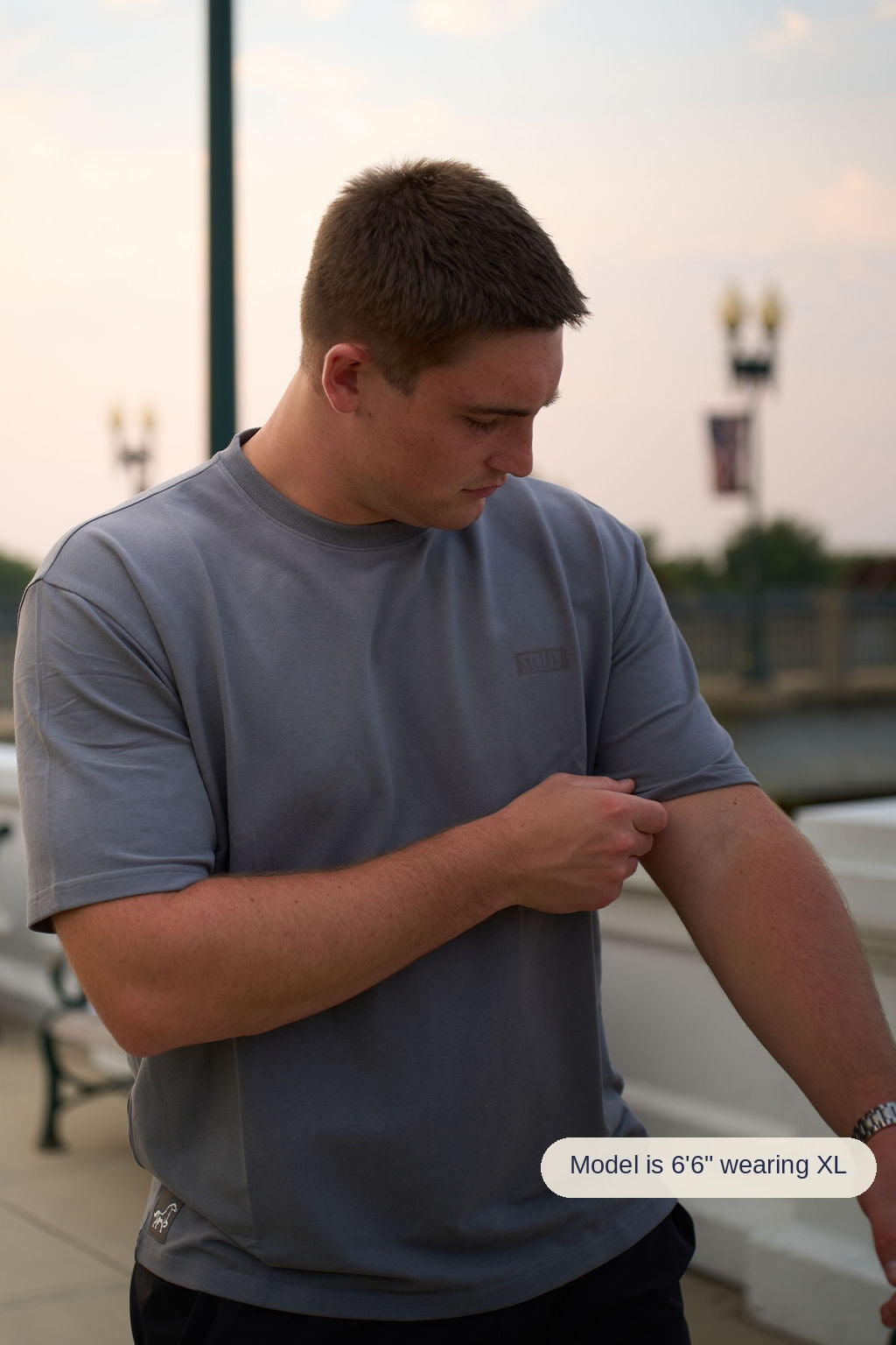 A man wearing a gray athletic t-shirt with a color-blocked design, standing outdoors near a white railing.