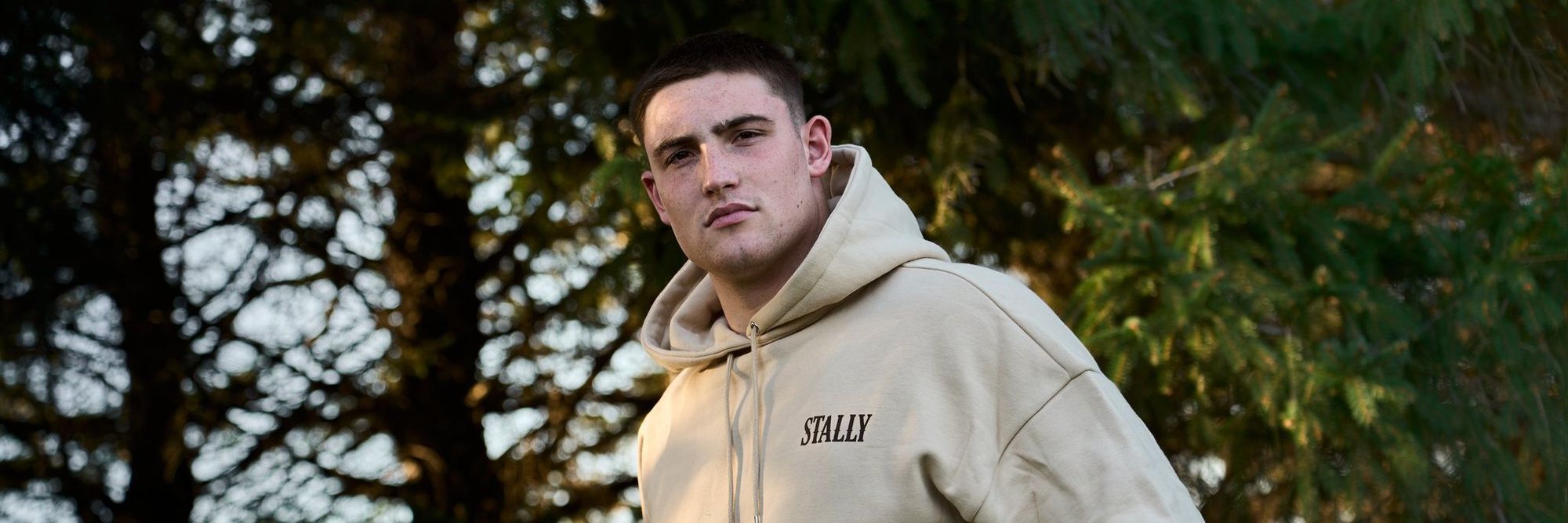 A man in a Saddlewood Stally Draft hoodie under evergreen trees