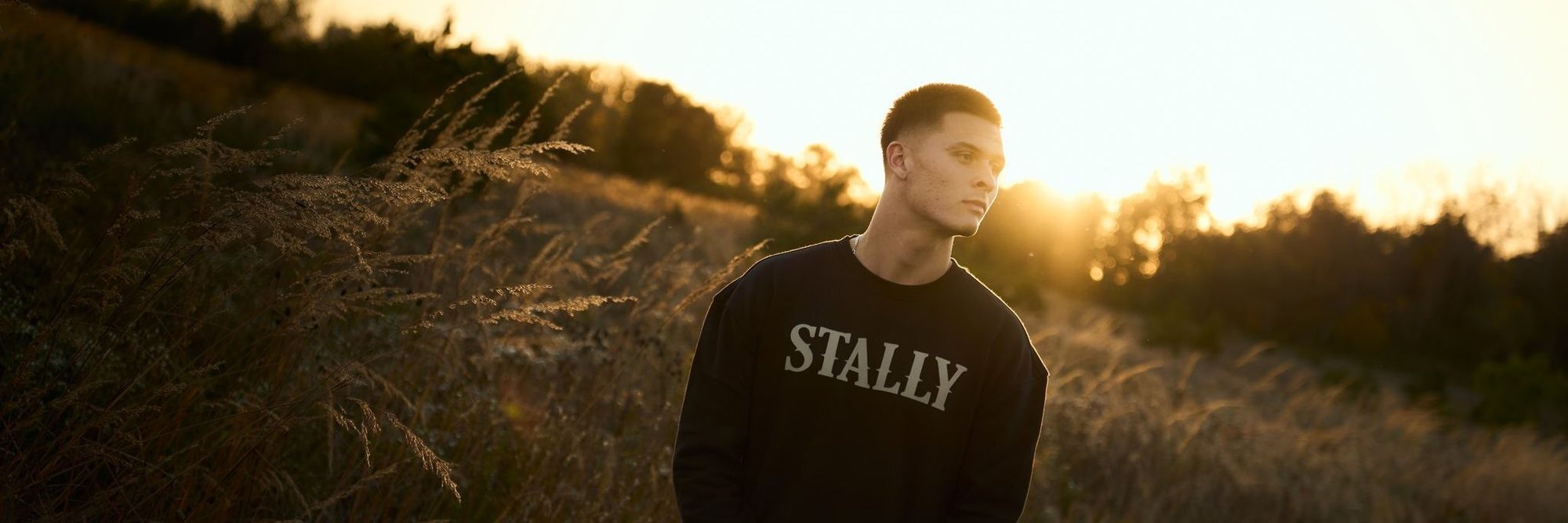 A man in a Coal Black Stally crew in tall grass at sunset